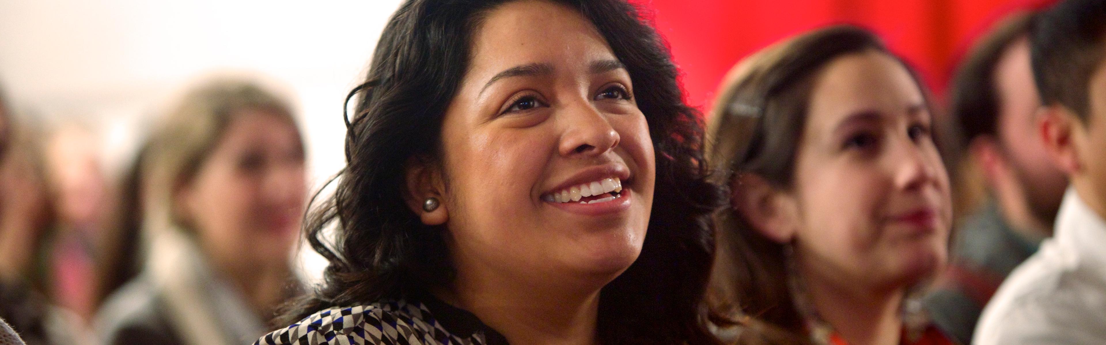 A smiling young woman watches a presentation in her Colorado teacher prep program