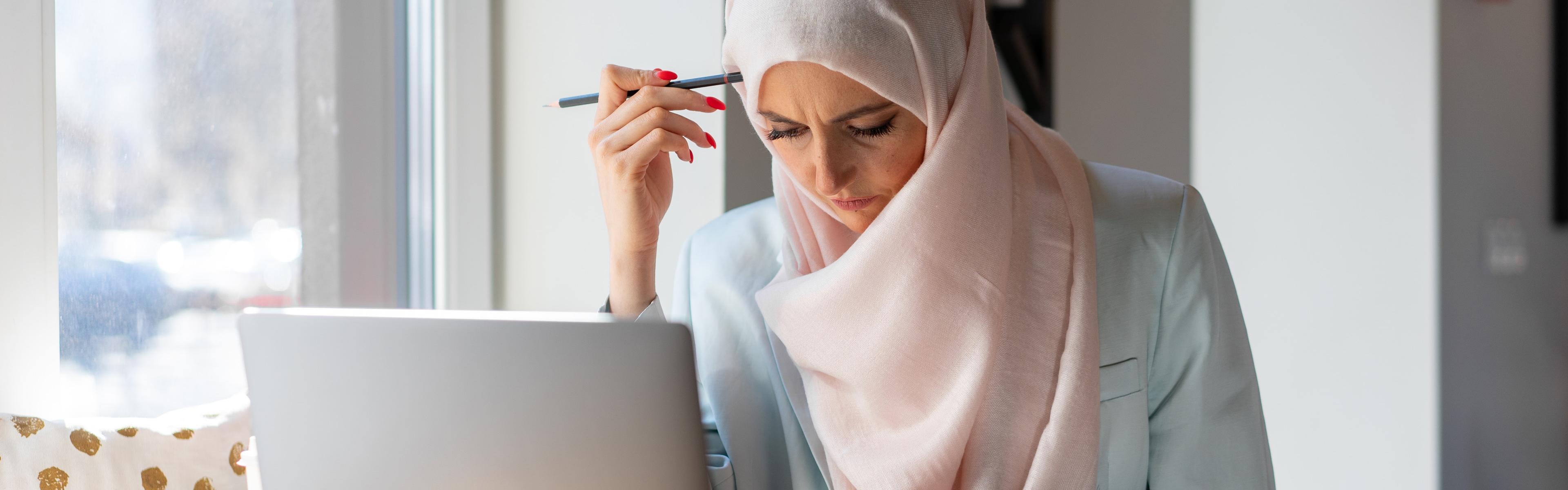 A Muslim woman sits at a laptop studying for her Colorado content area assessment.